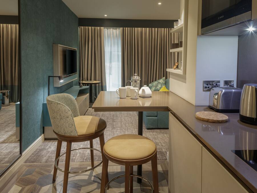Una habitación de hotel moderna con zona de comedor, cocina equipada con electrodomésticos Bosch y televisión.