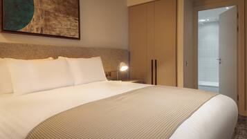 Habitación de hotel con una cama grande, una mesita de noche con lámpara, un armario y un baño visible a través de una puerta abierta.
