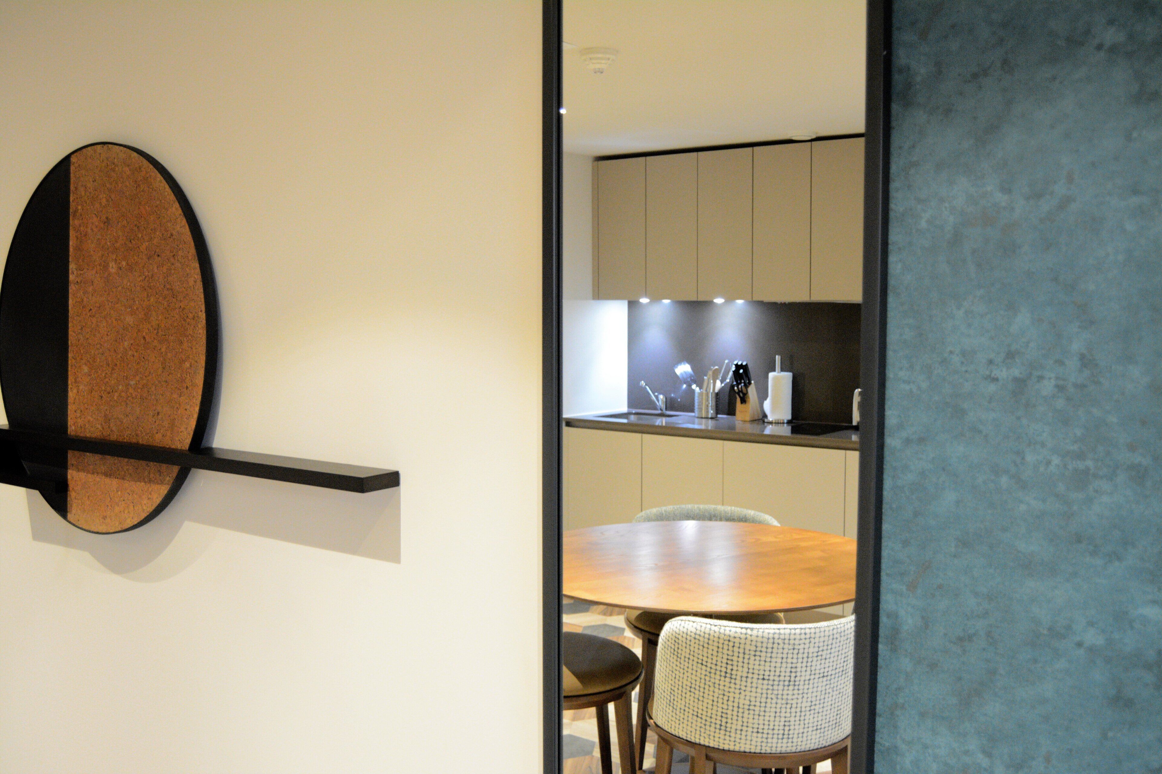 Een modern interieur met een prikbordwand, een houten eettafel en een keukenhoek.