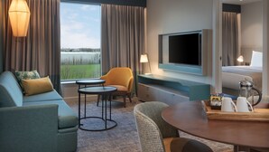 A modern hotel room with a sofa, armchair, round table, and a TV. - Staybridge Suites London Heathrow - Bath Road by IHG (West Drayton)