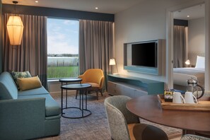Une chambre d’hôtel moderne équipée d’un canapé, d’un fauteuil, d’une table ronde et d’un téléviseur.