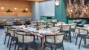 A restaurant with multiple dining tables and chairs, wooden paneling on the walls, and a green accent wall with a tropical mural. - Staybridge Suites London Heathrow - Bath Road by IHG (West Drayton)