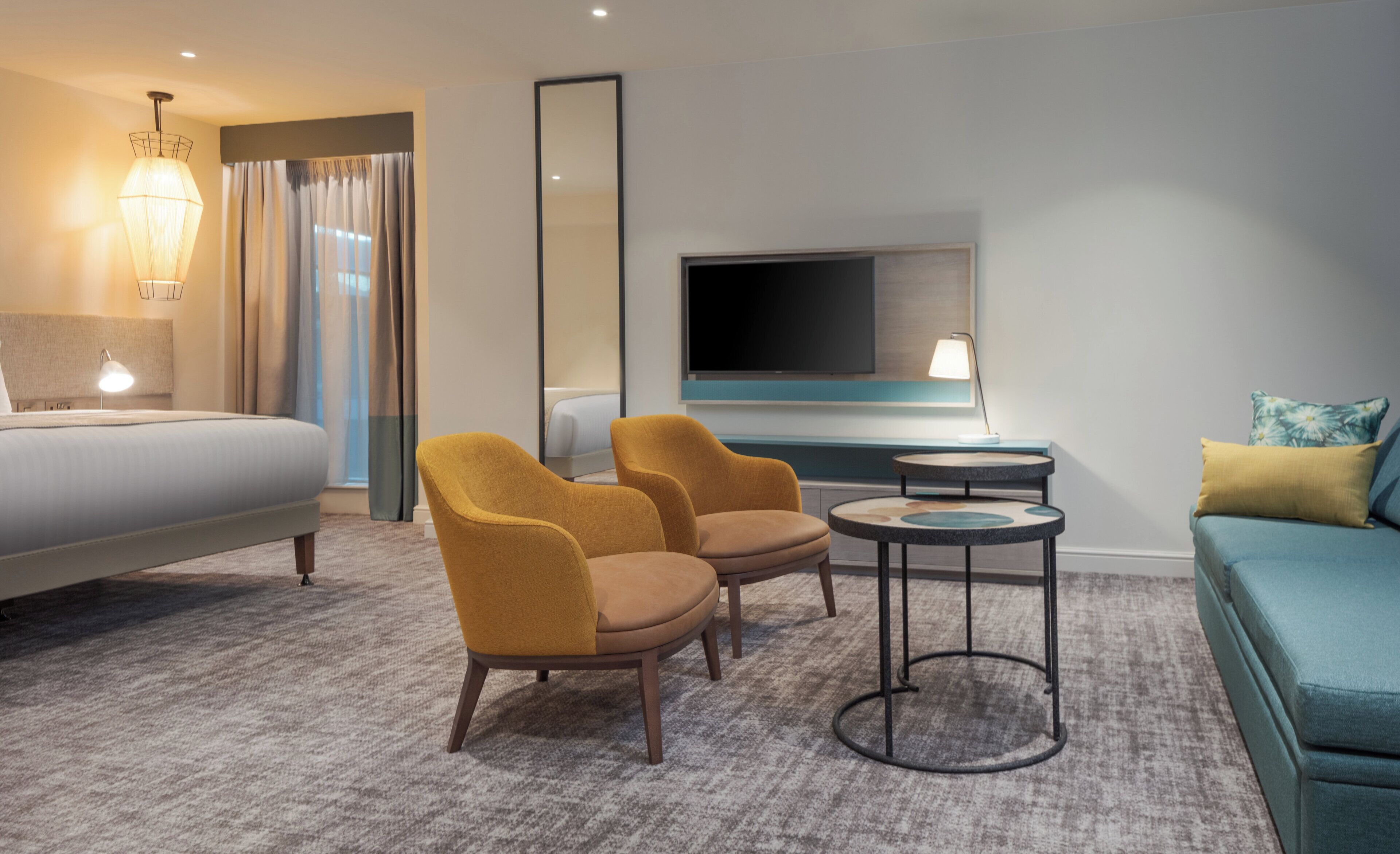 Een hotelkamer met een bed, twee fauteuils, een kleine ronde tafel, een bank, een televisie en een lamp.