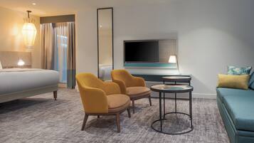 Quarto de hotel com cama, duas poltronas, mesa redonda pequena, sofá, televisão e abajur.