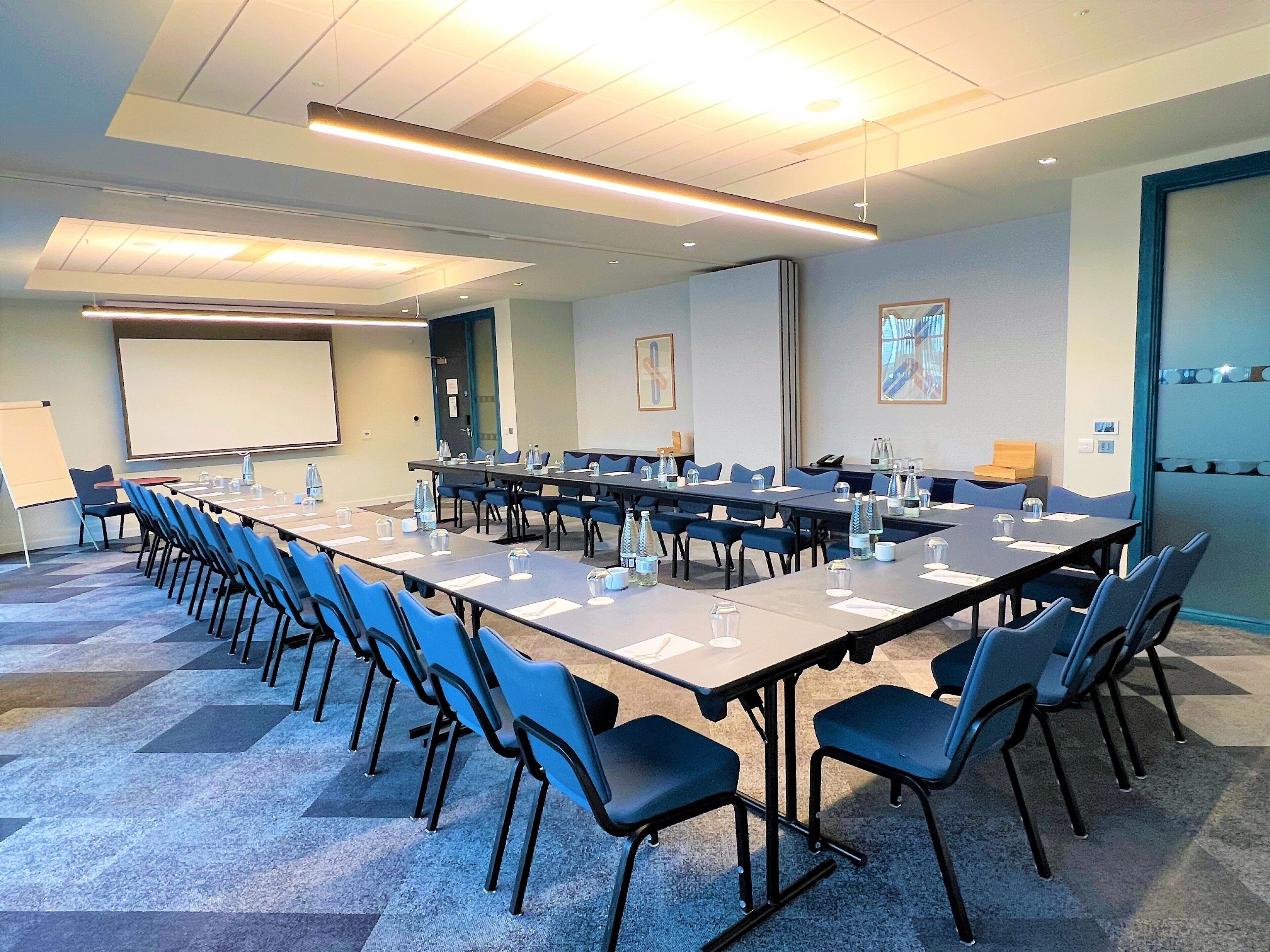 A conference room with a long table, chairs, a projector screen, and a whiteboard.