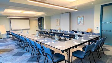 Un salón de conferencias con una larga mesa, sillas, una pantalla de proyector y una pizarra.