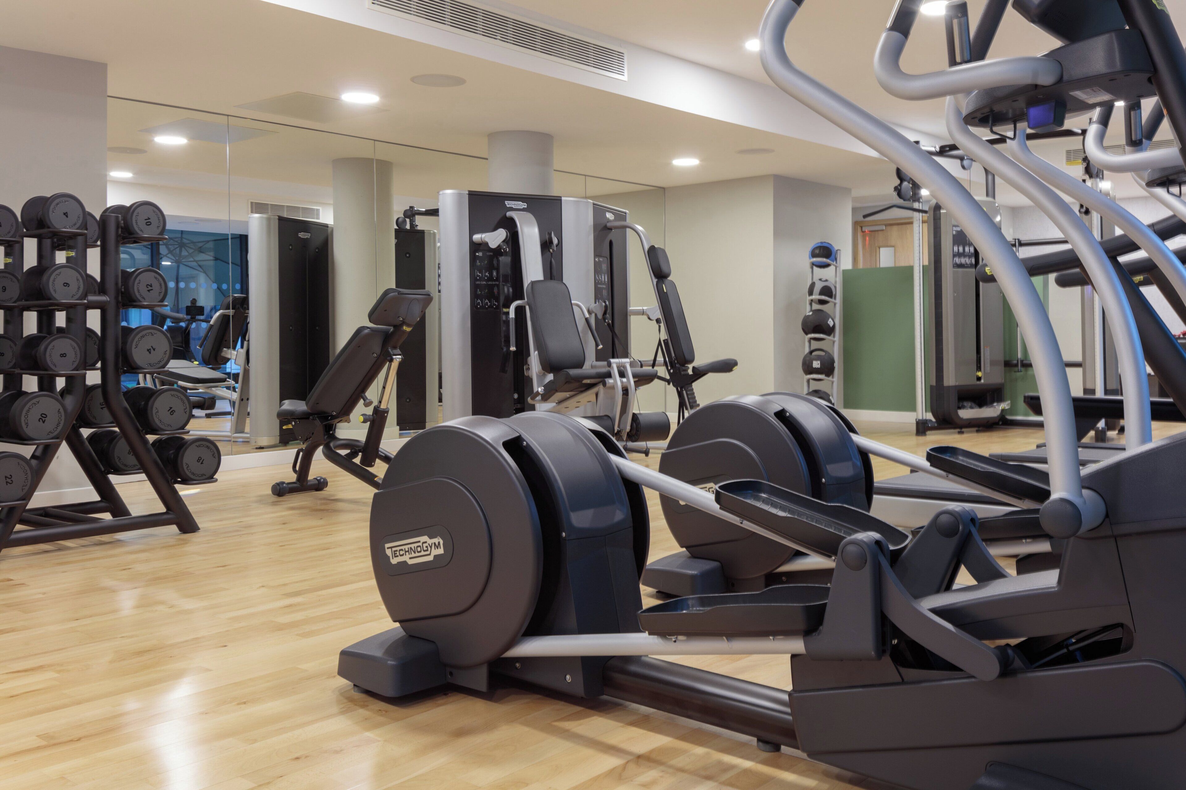 Un gimnasio con máquinas de cardio, equipo de levantamiento de pesas y un espejo grande.