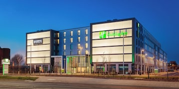 Un moderno hotel Holiday Inn con fachada de vidrio, varios pisos y un logotipo verde destacado.