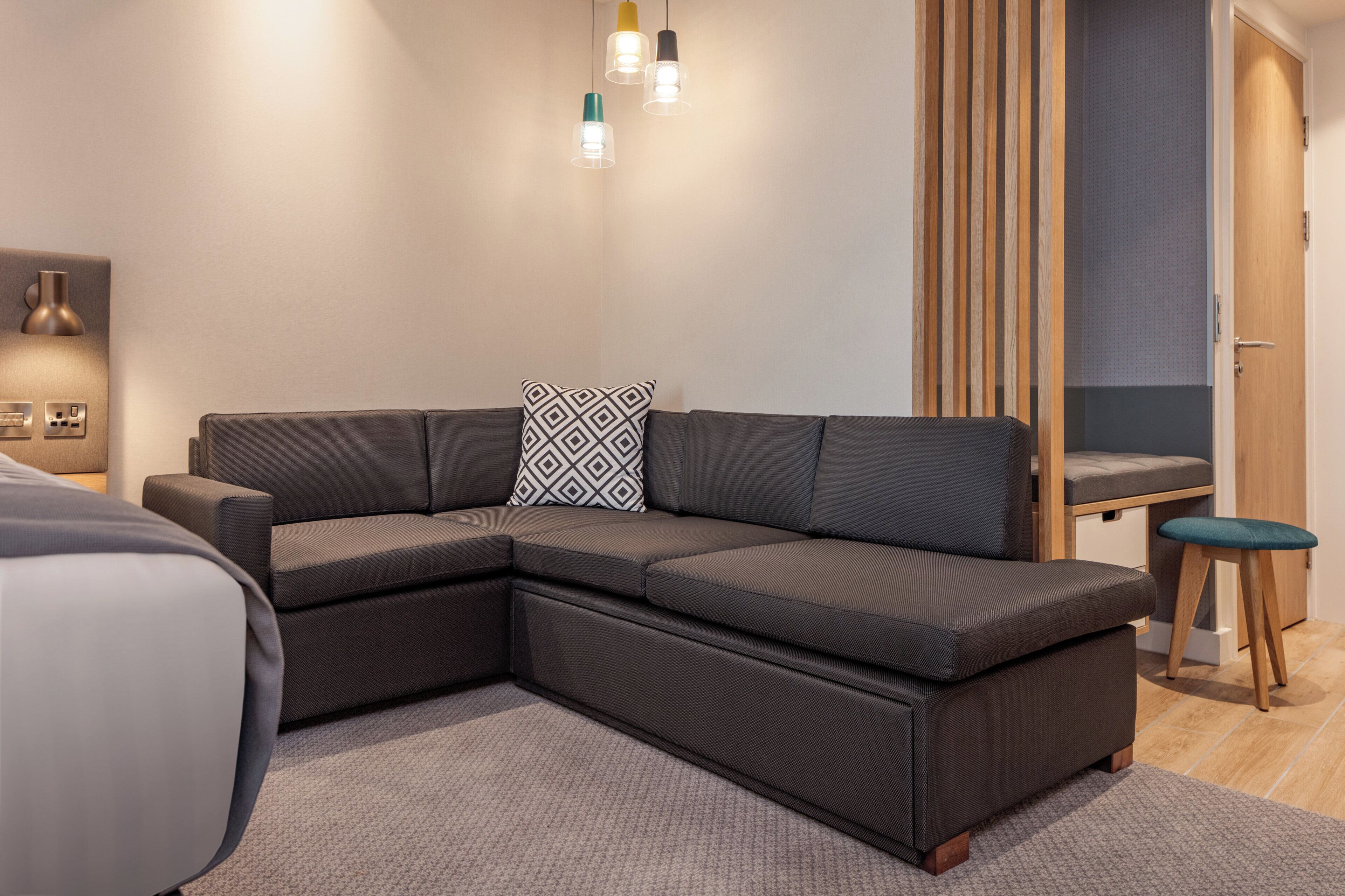 A modern living room with a sectional sofa, a small stool, and a wall-mounted light fixture.