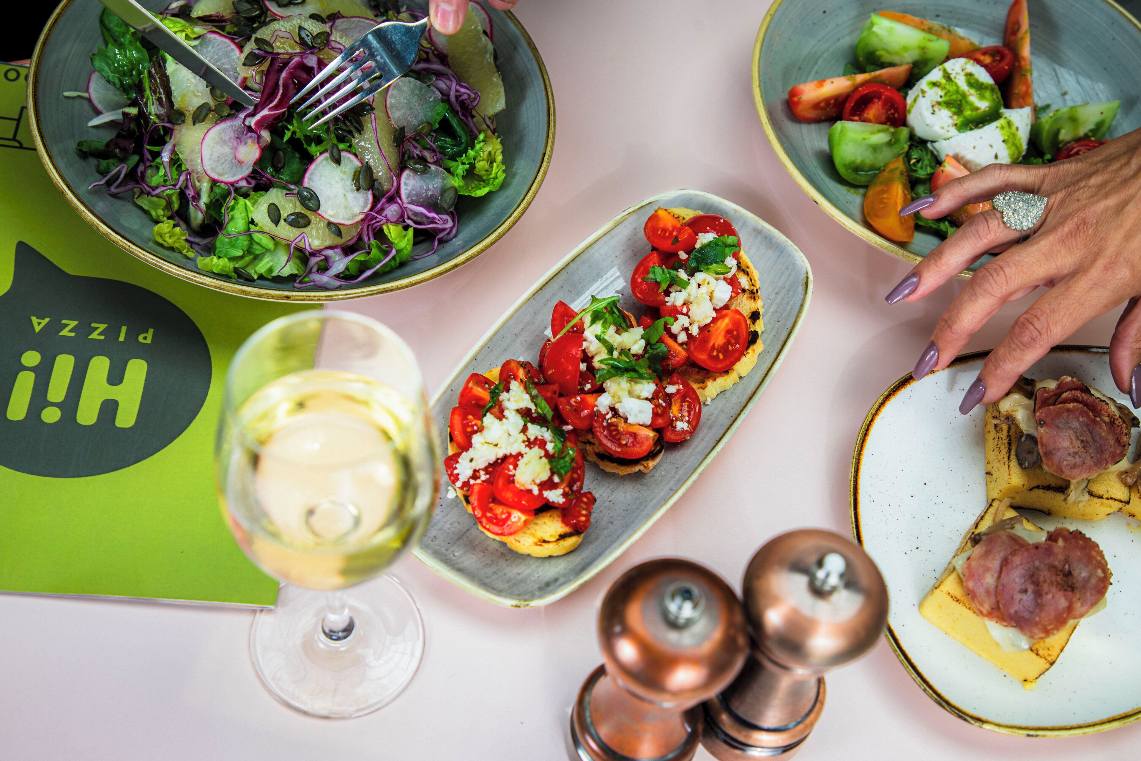 A table with various dishes, a glass of white wine, and a person's hand with a ring.