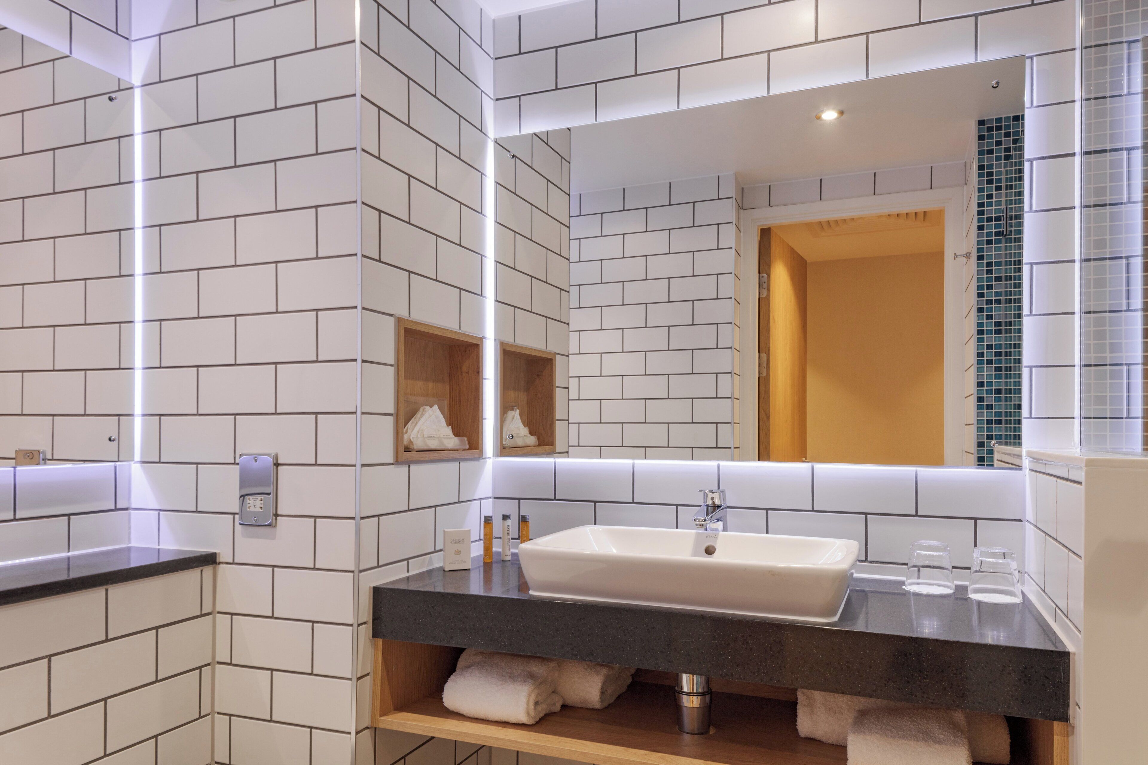 A modern bathroom with a white tiled wall, a black countertop, a sink, and a mirror.