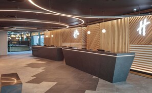 A modern reception area with a curved reception desk, wooden slatted walls, and pendant lighting. - Holiday Inn London Heathrow - Bath Road by IHG (West Drayton)