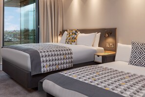 A hotel room with two beds, a large window with curtains, a nightstand, and a lamp. - Holiday Inn London Heathrow - Bath Road by IHG (West Drayton)