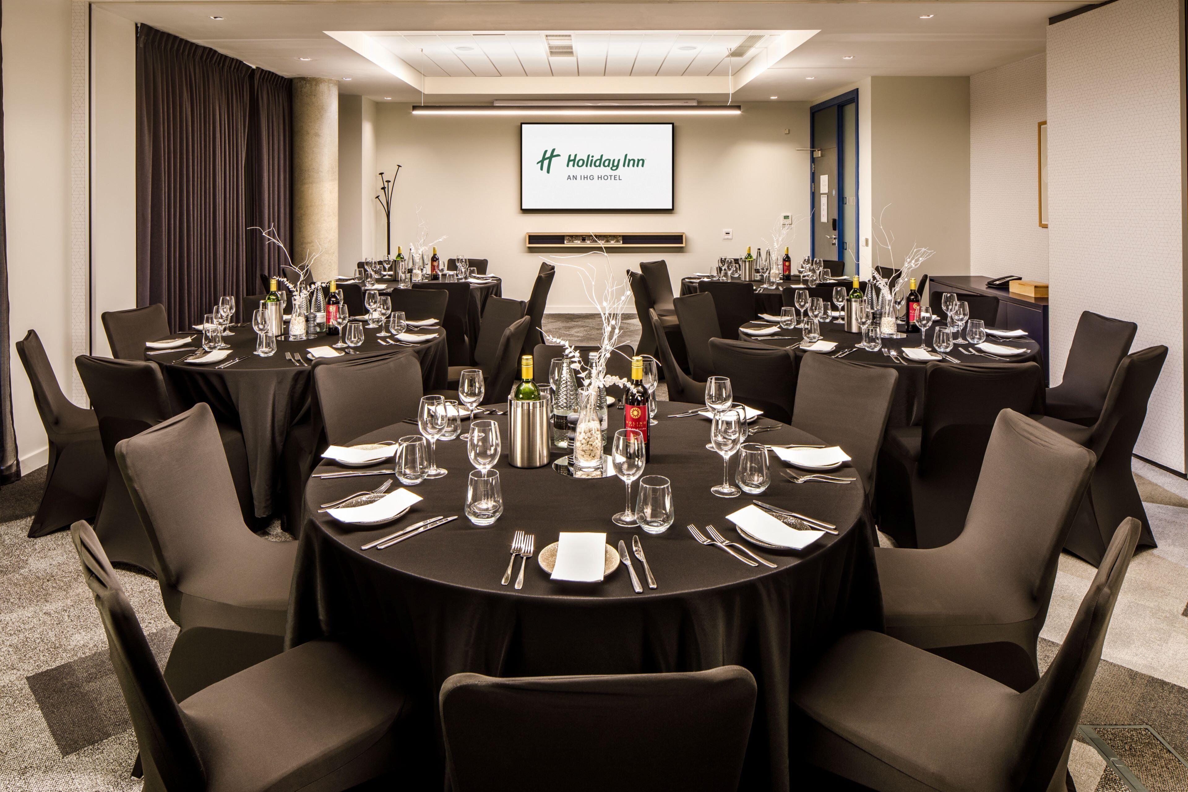 A conference room with round tables, black tablecloths, and chairs.