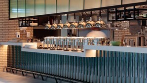 A modern kitchen with a brick wall, a stainless steel countertop, and a variety of kitchen appliances and utensils. - Holiday Inn London Heathrow - Bath Road by IHG (West Drayton)