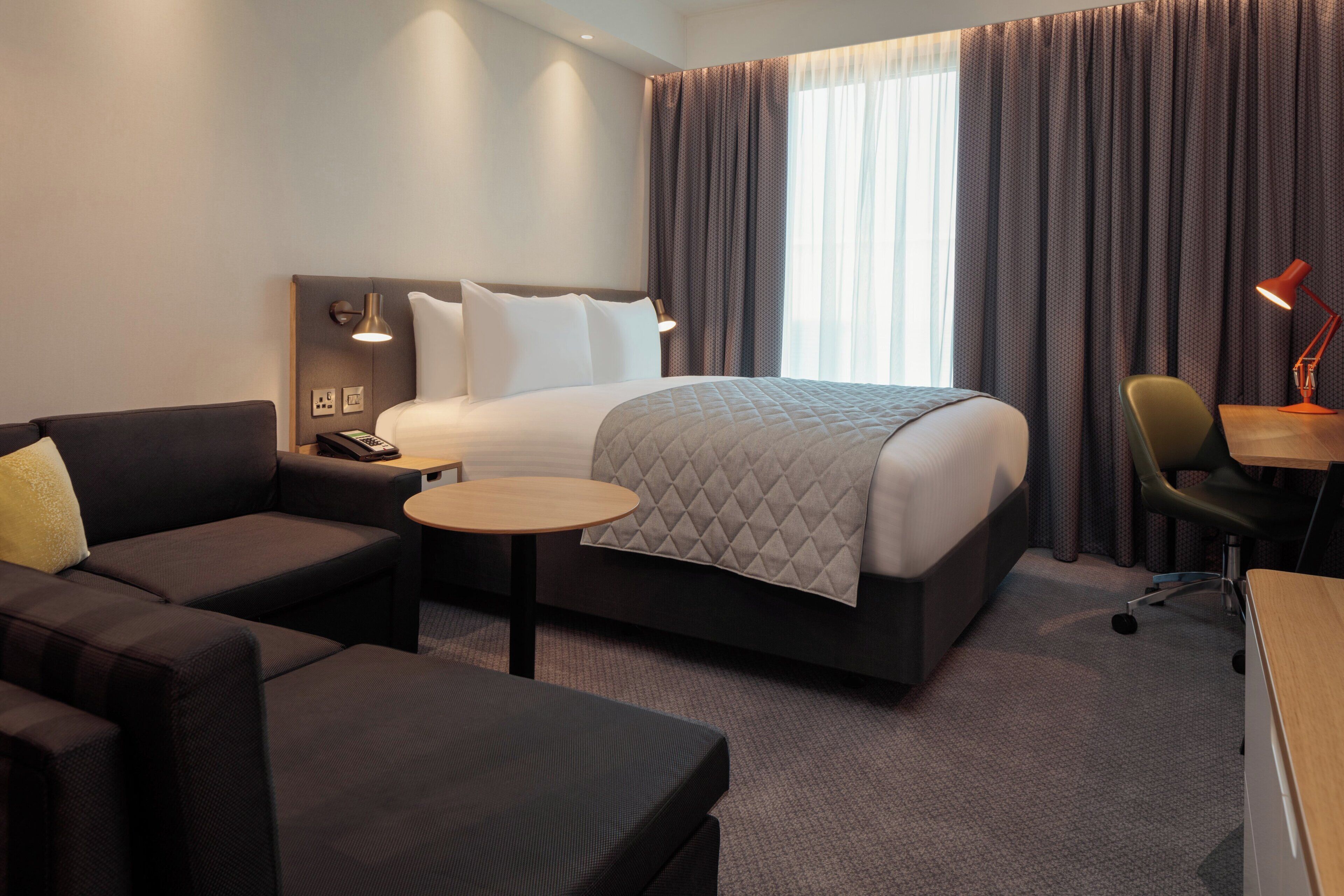 A hotel room with a bed, a desk, a chair, a sofa, and a small table.