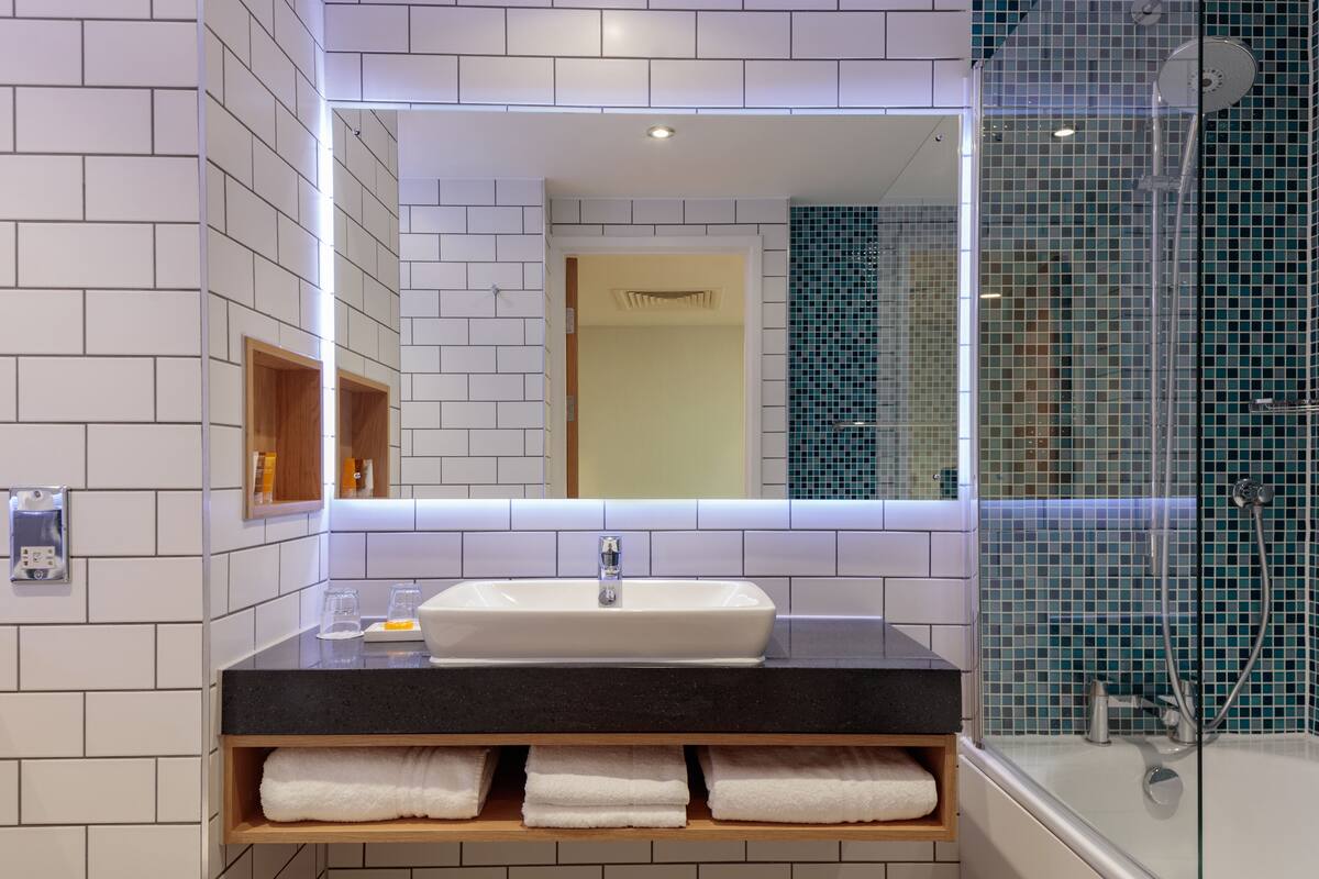 A modern bathroom with a white tiled wall, a black countertop, a white sink, and a glass-enclosed shower area.