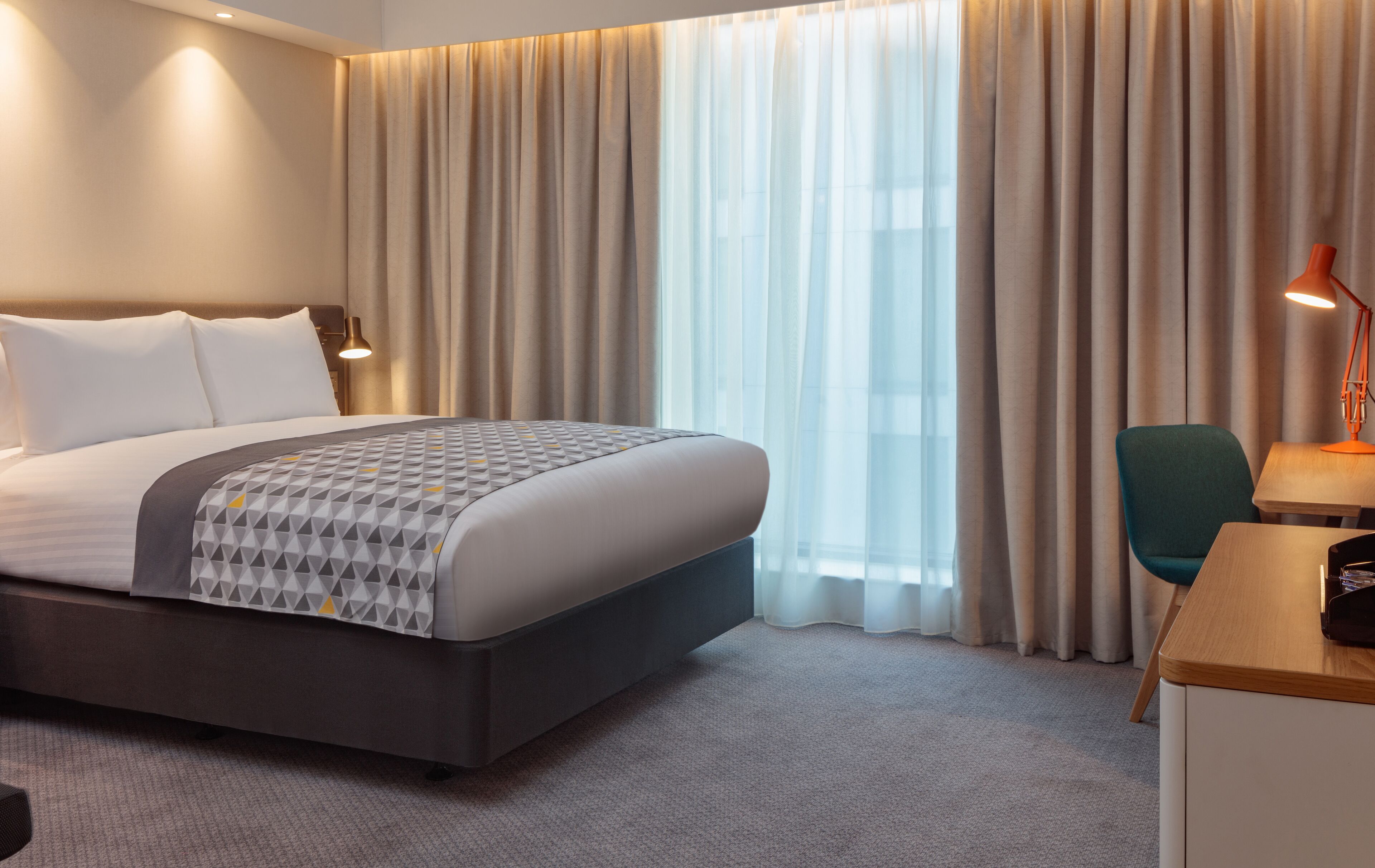 Una habitación de hotel con una cama grande, un escritorio, una silla y una ventana con cortinas.