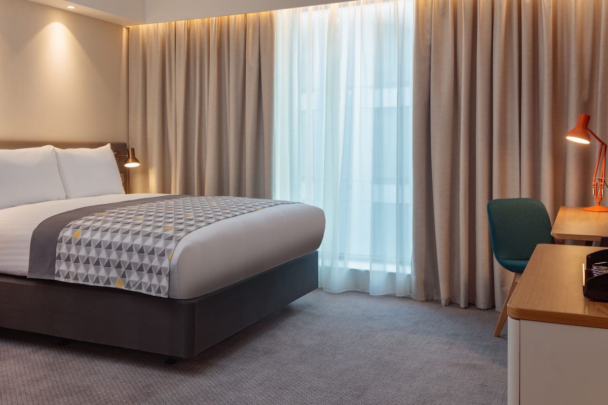 A hotel room with a large bed, a desk, a chair, and a window with curtains.