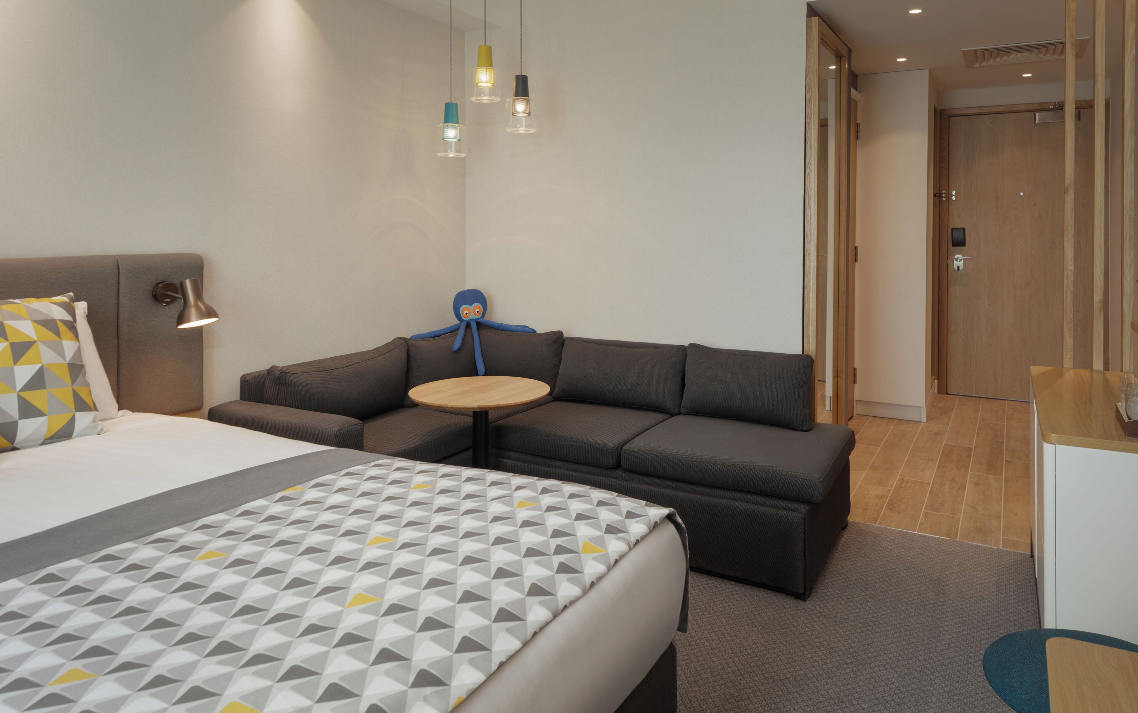 A hotel room with a bed, a sofa, a small round table, and a blue octopus decoration.