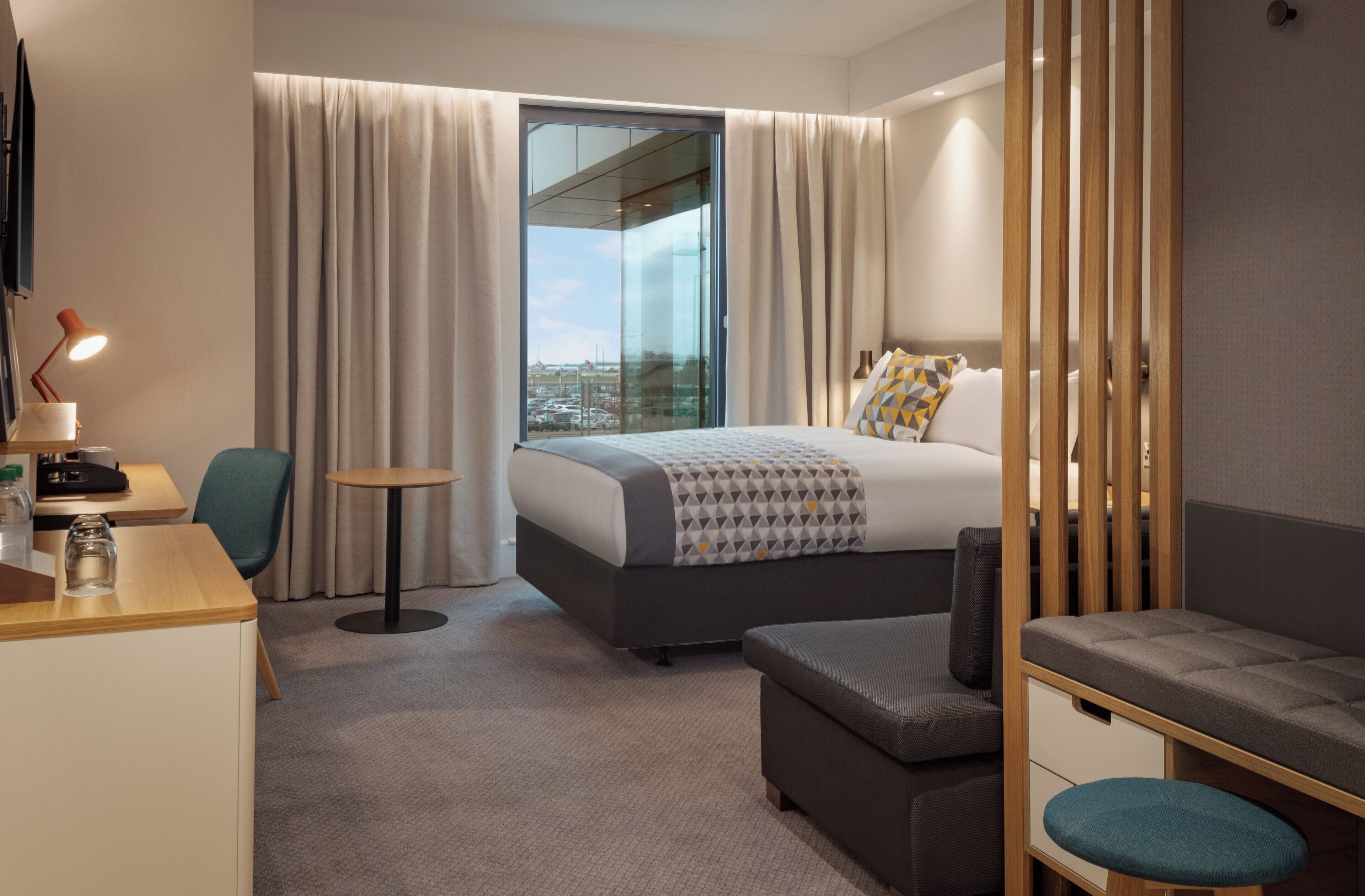 Una habitación de hotel con cama, escritorio, silla, una mesita y vistas al exterior.