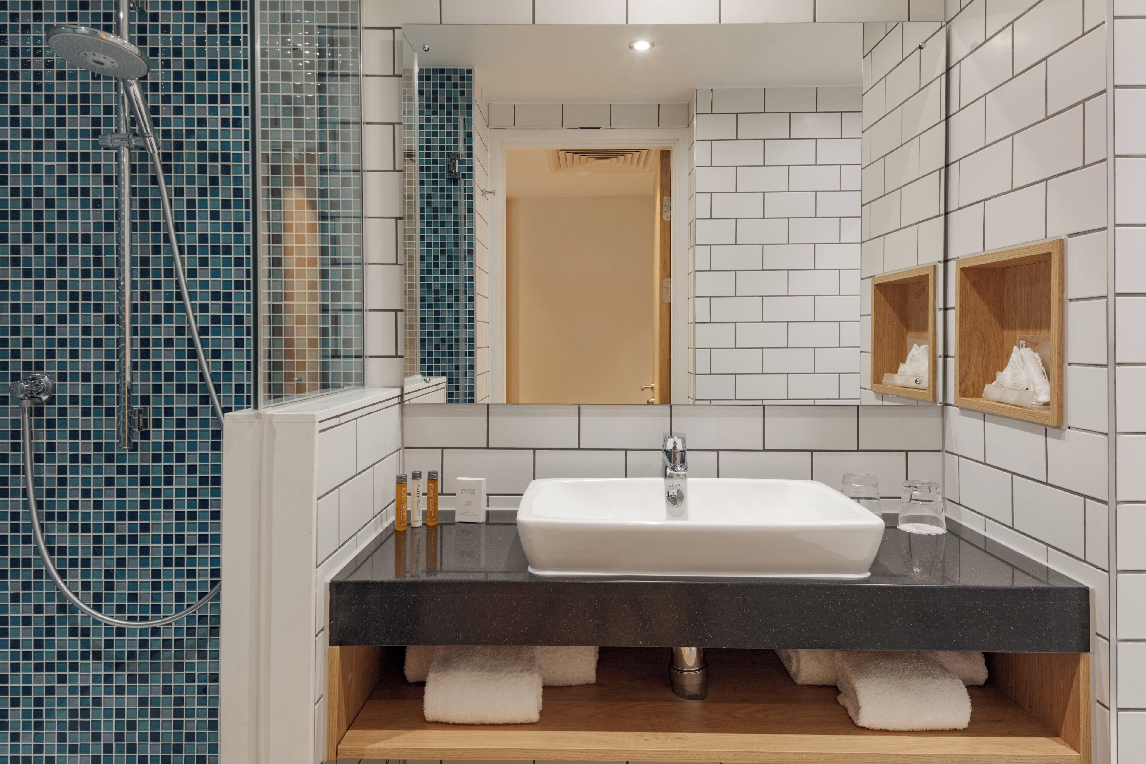 A modern bathroom with a white sink, a shower, and a mirror.