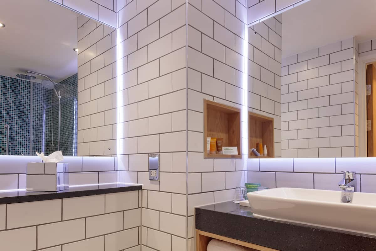 A modern bathroom with white tiled walls, a black countertop, a sink, and a mirror.