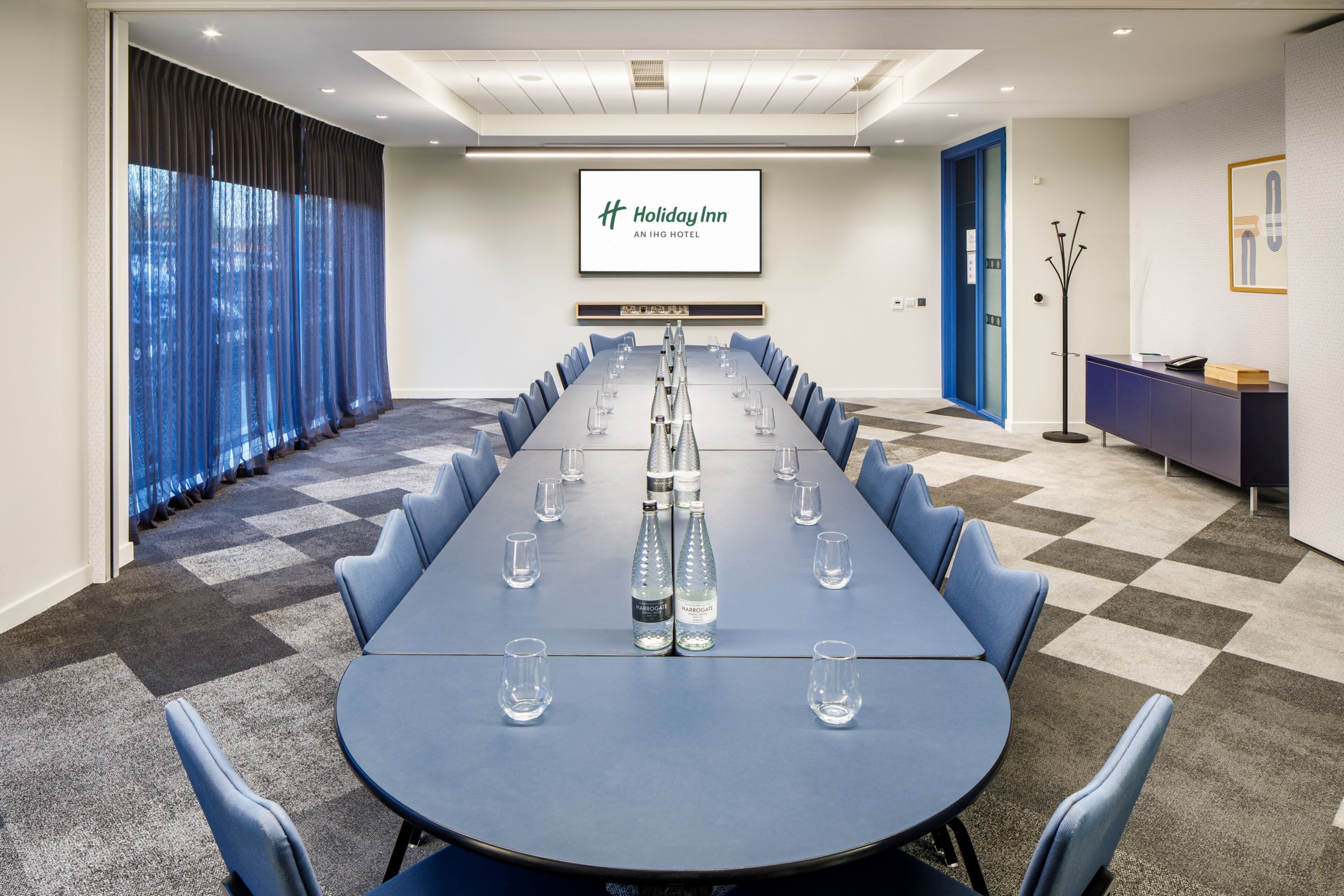 A conference room with a long table, chairs, and a screen displaying the Holiday Inn logo.