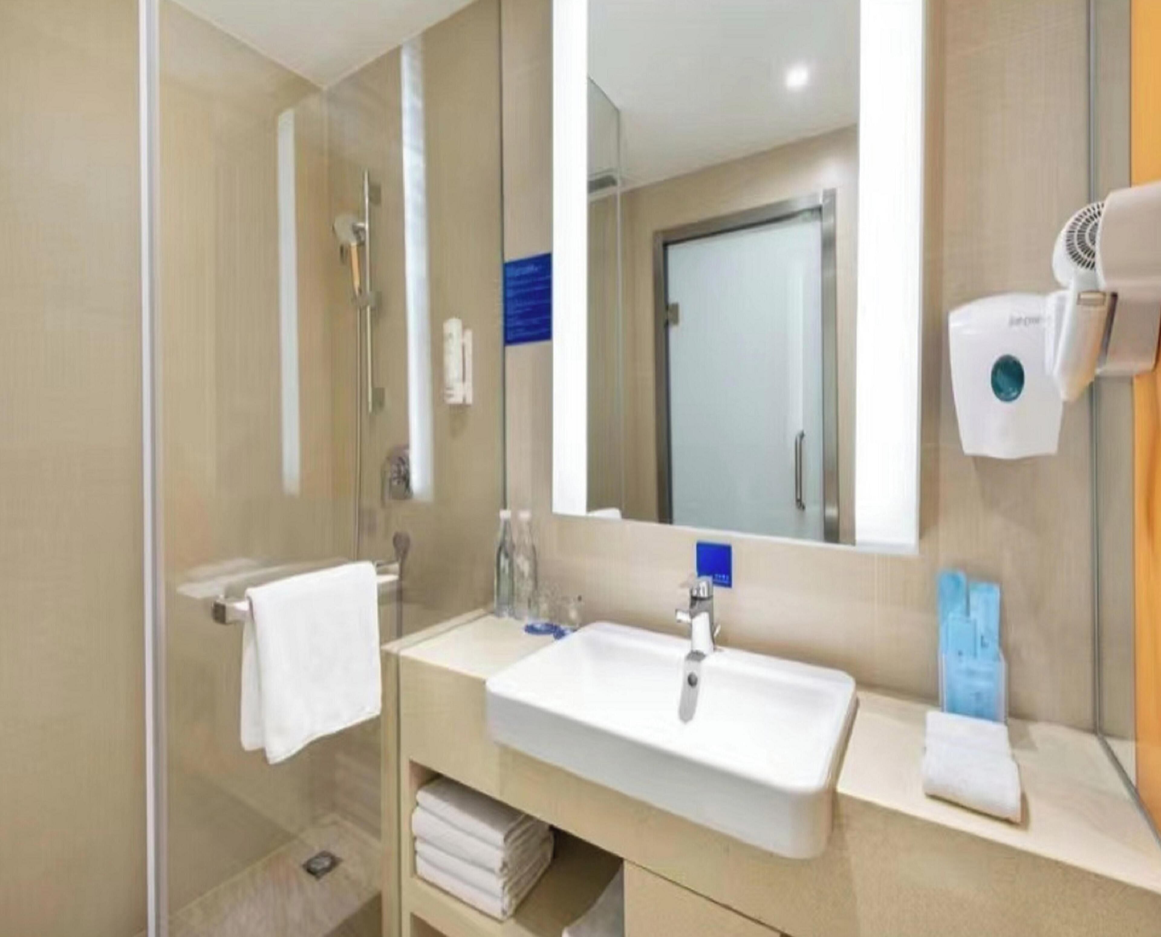 A modern bathroom with a glass shower enclosure, a sink with a mirror, and a hairdryer mounted on the wall.