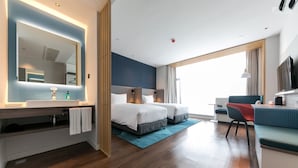 A modern hotel room with a large bed, a desk, a chair, a TV, and a bathroom with a mirror and sink.