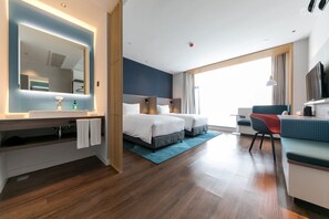 A modern hotel room with a large bed, a desk, a chair, a TV, and a bathroom with a mirror and sink.