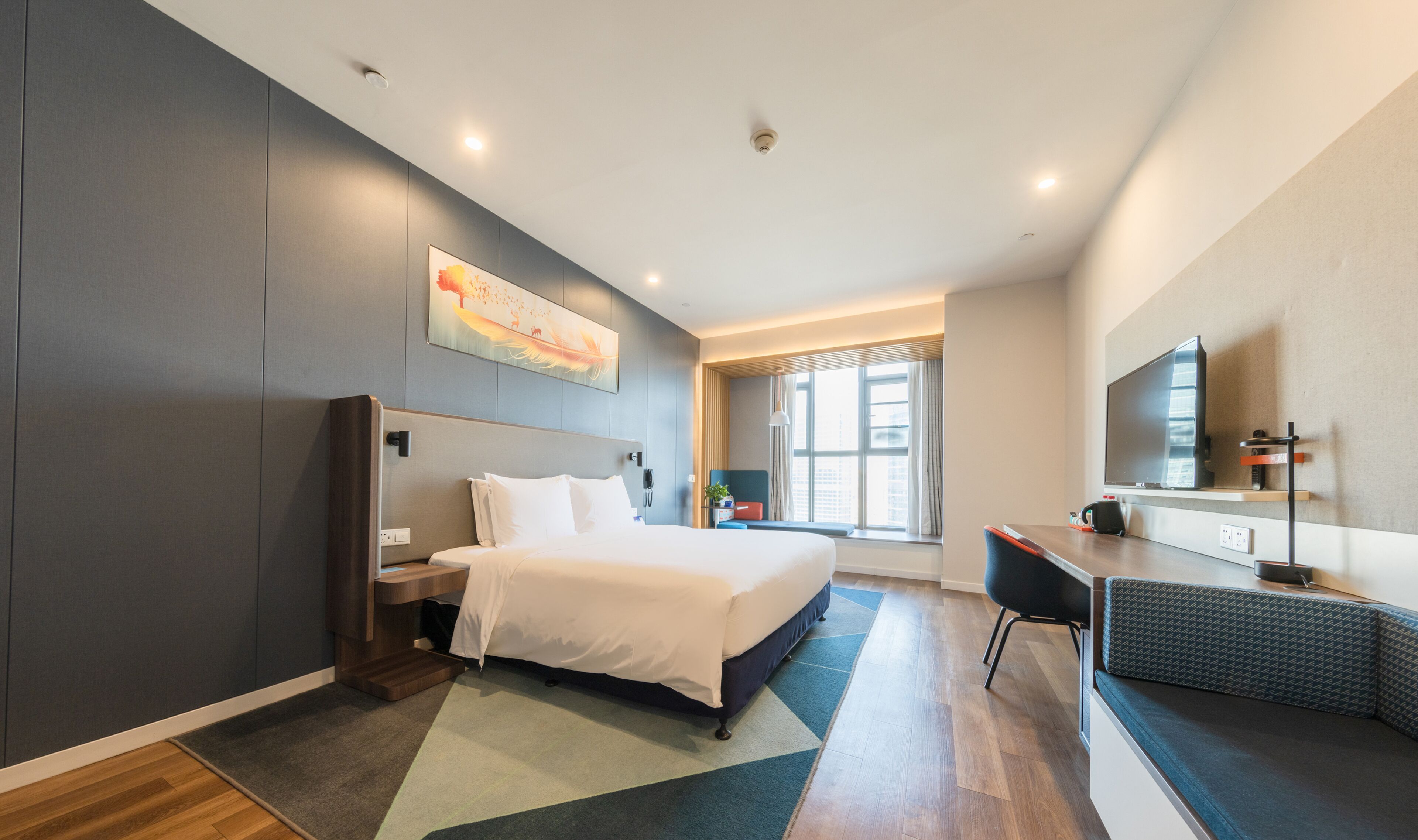 A modern hotel room with a large bed, a desk, a chair, a TV, and a window with curtains.