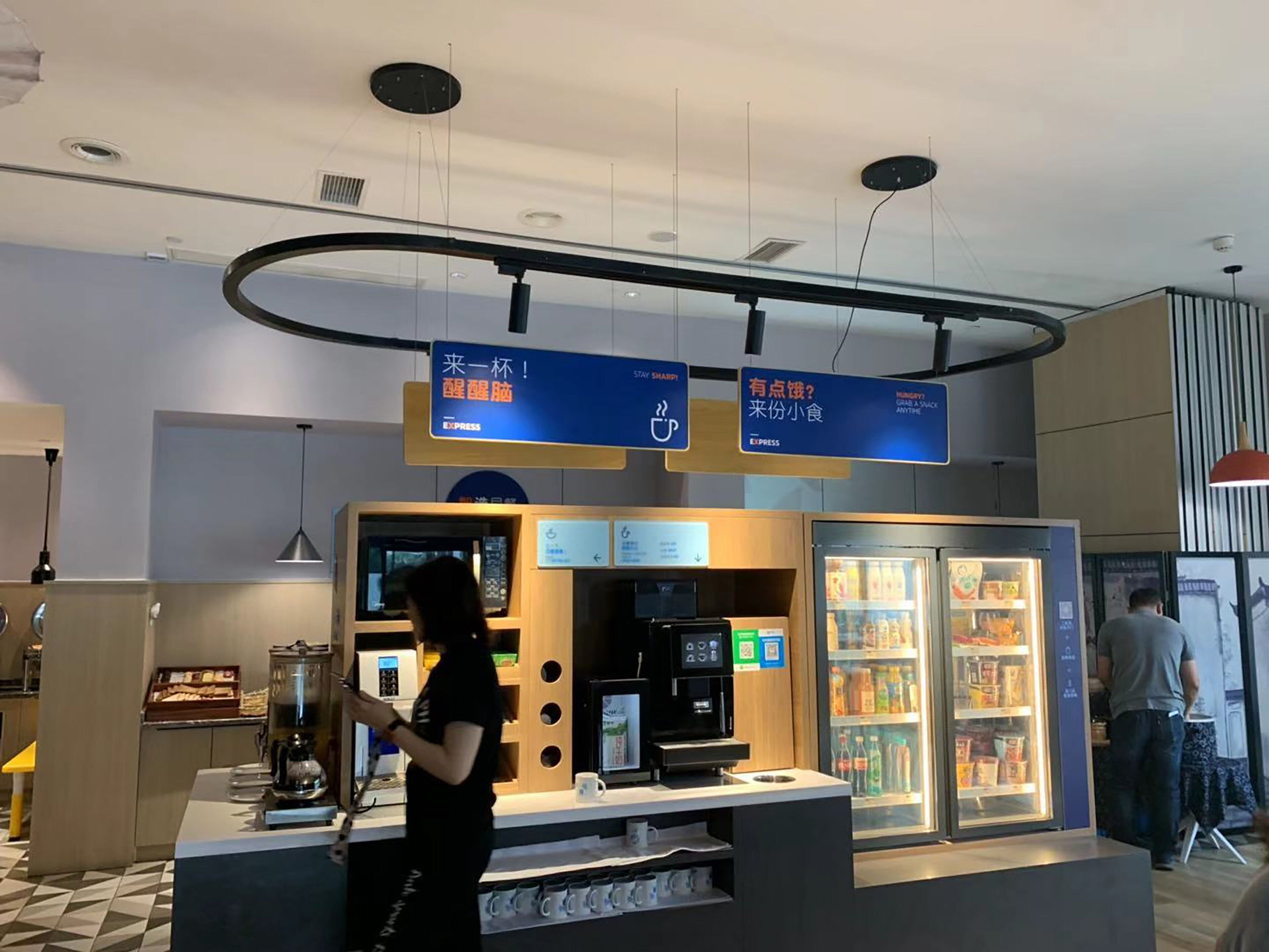 En selvbetjeningsstation med kaffemaskine, nedkølet drikkeautomat og digital menu.