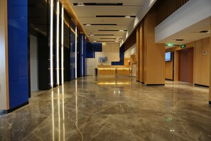 Un moderno vestíbulo de hotel con piso de mármol, una recepción y una pantalla de televisión.