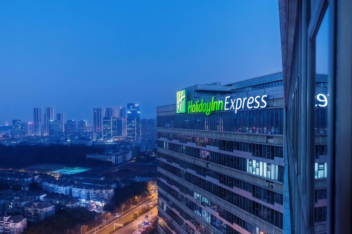 A Holiday Inn Express building with a modern glass facade, surrounded by a cityscape at dusk.