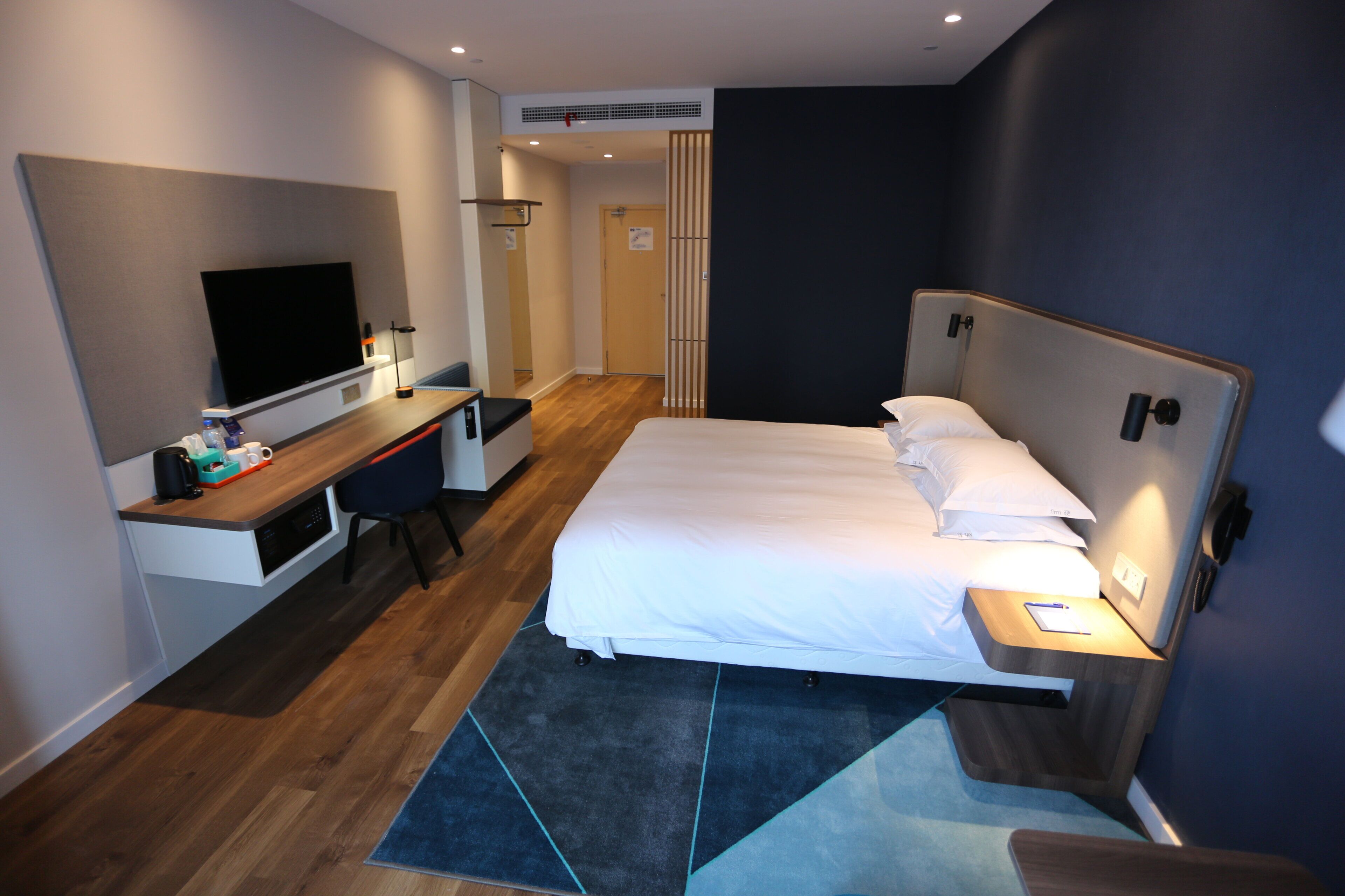 A hotel room with a bed, a desk, a television, and a bathroom visible through an open door.