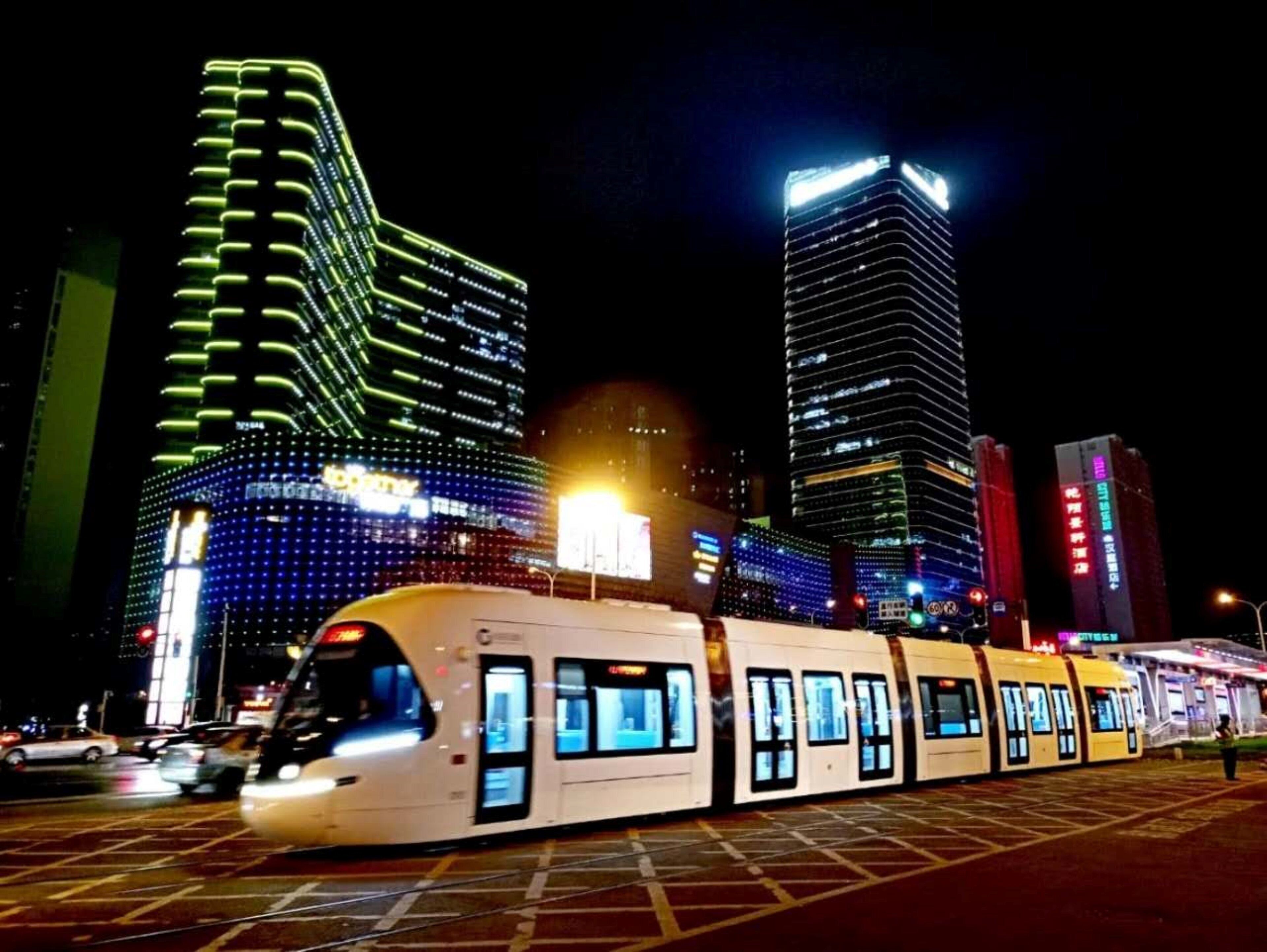 A modern train station at night with illuminated buildings in the background.