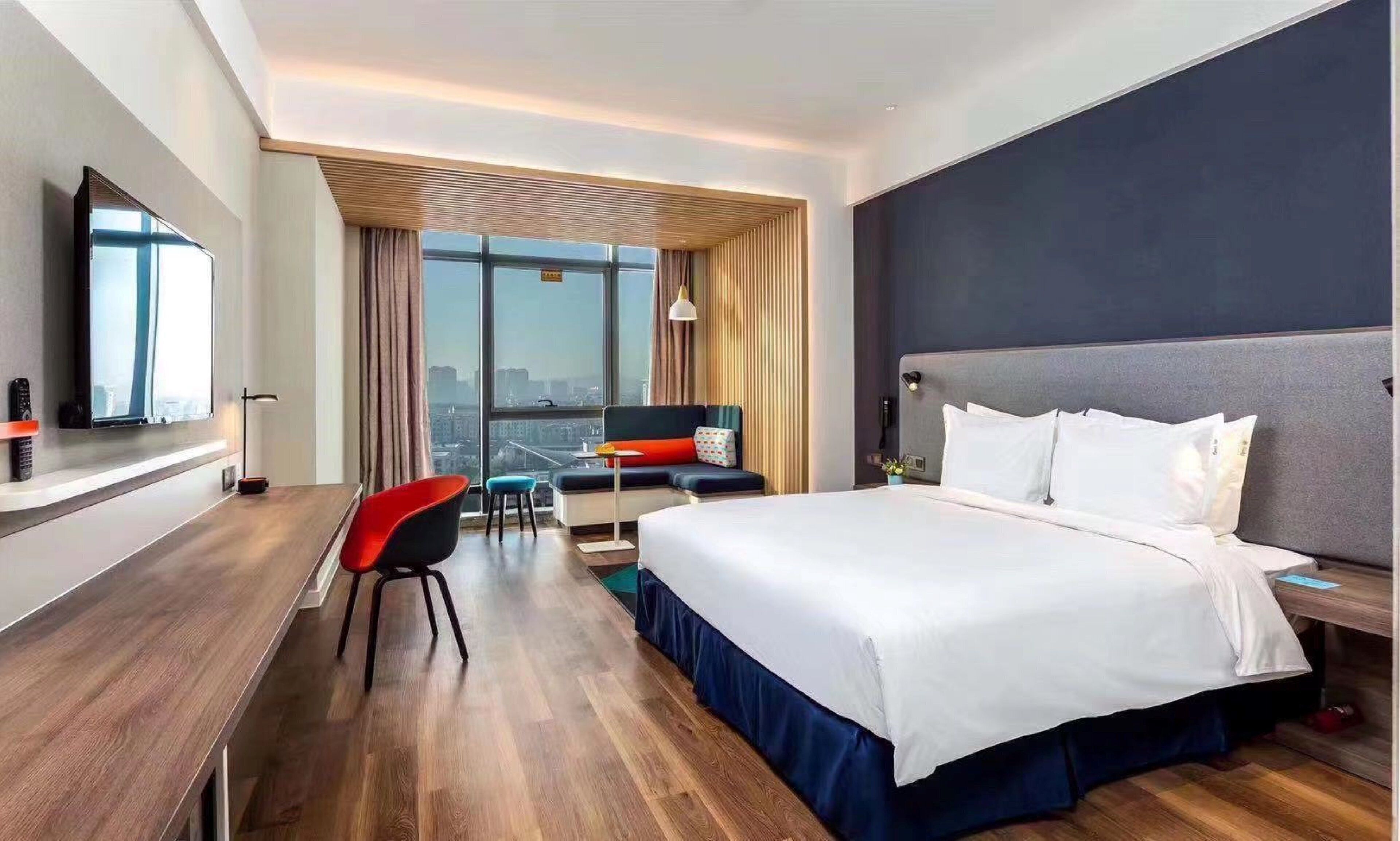 Ett modernt hotellrum med en stor säng, ett skrivbord och utsikt över staden.