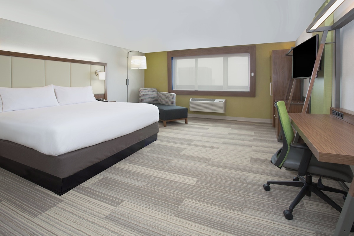 A hotel room with a large bed, a desk, a chair, a television, and a window.