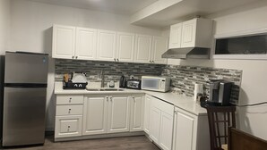 A modern kitchen with white cabinets, a stainless steel refrigerator, a microwave, and a coffee maker. - Starting Point Family House (Victoria)