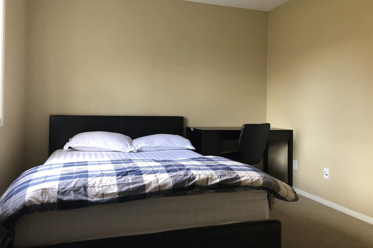 A bedroom with a bed, a desk, and a chair.