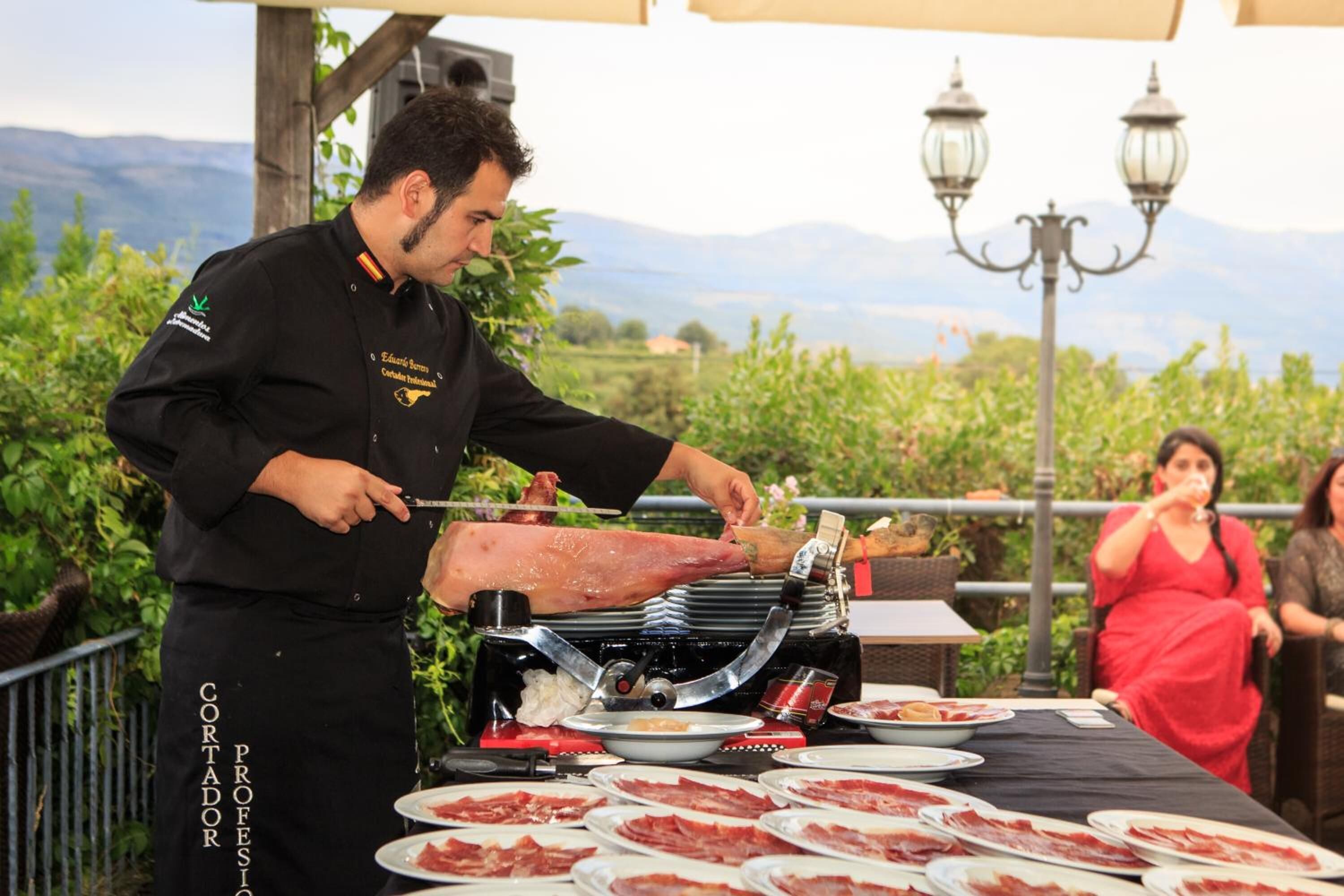 A chef carving meat on a grill outdoors with a scenic mountain view in the background.