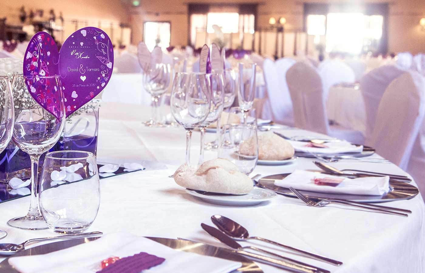 Una mesa de banquete dispuesta con copas de vino, platos y panecillos, con adornos con forma de corazón sobre el mantel.