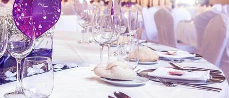 Una mesa de banquete dispuesta con copas de vino, platos y panecillos, con adornos con forma de corazón sobre el mantel.