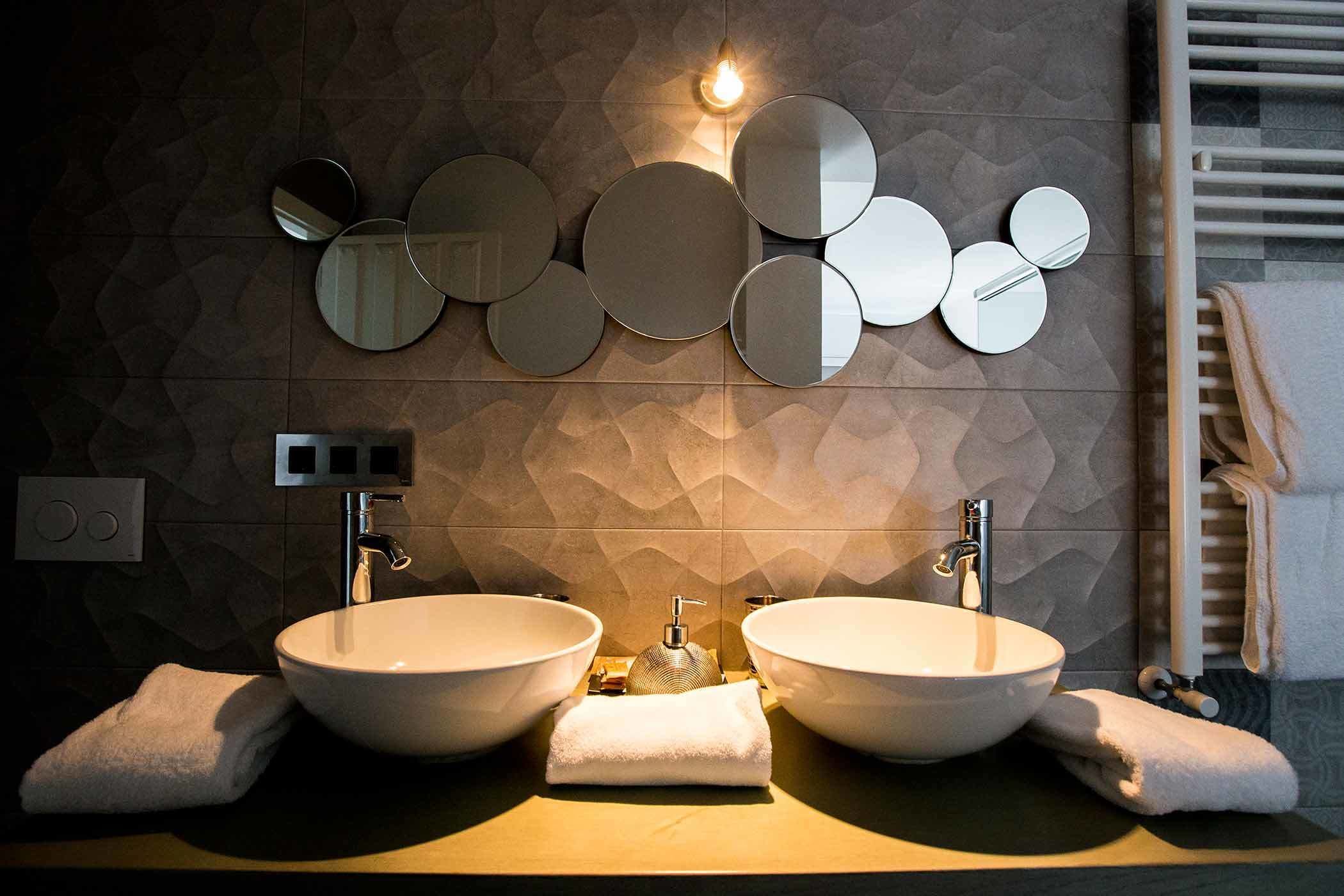 Un baño moderno con dos lavamanos grandes de color blanco, un espejo montado en la pared y un perchero para toallas.