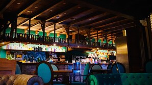 A bar area with wooden beams and a balcony overlooking the bar. There are multiple bottles and glasses on the shelves. - Villa Xarahiz (Jaraíz de la Vera)