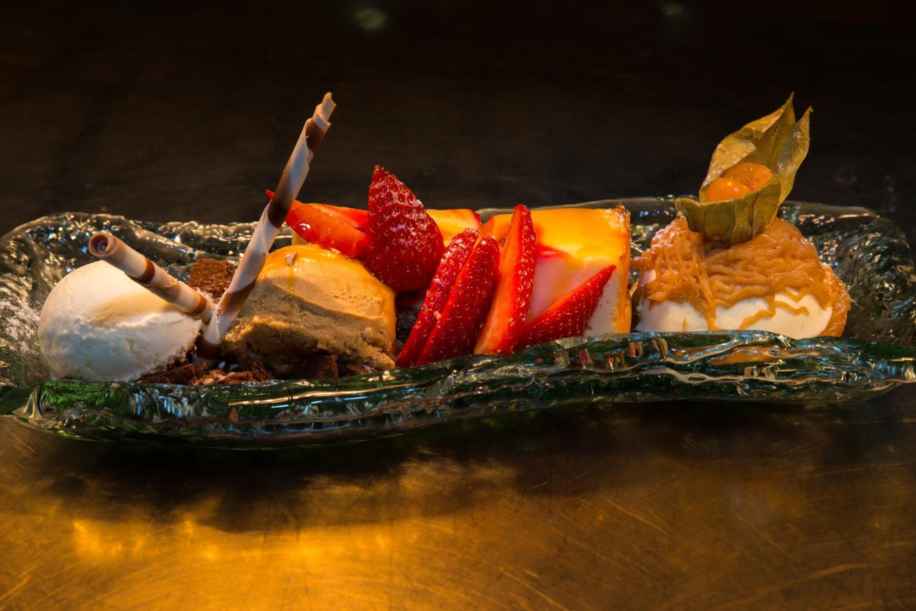 Una bandeja de postres con helado, fresas y un trozo de chocolate.