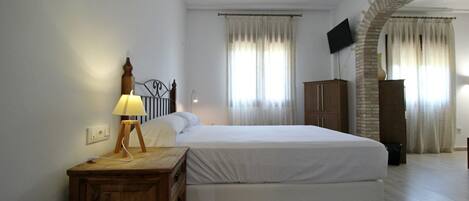 Un dormitorio con una cama, una mesita de noche de madera, una lámpara, un televisor montado en la pared y un arco de ladrillo.