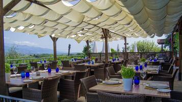 Un área de comedor al aire libre con sillas y mesas de mimbre, cubierta por un toldo y con vistas a un paisaje pintoresco.