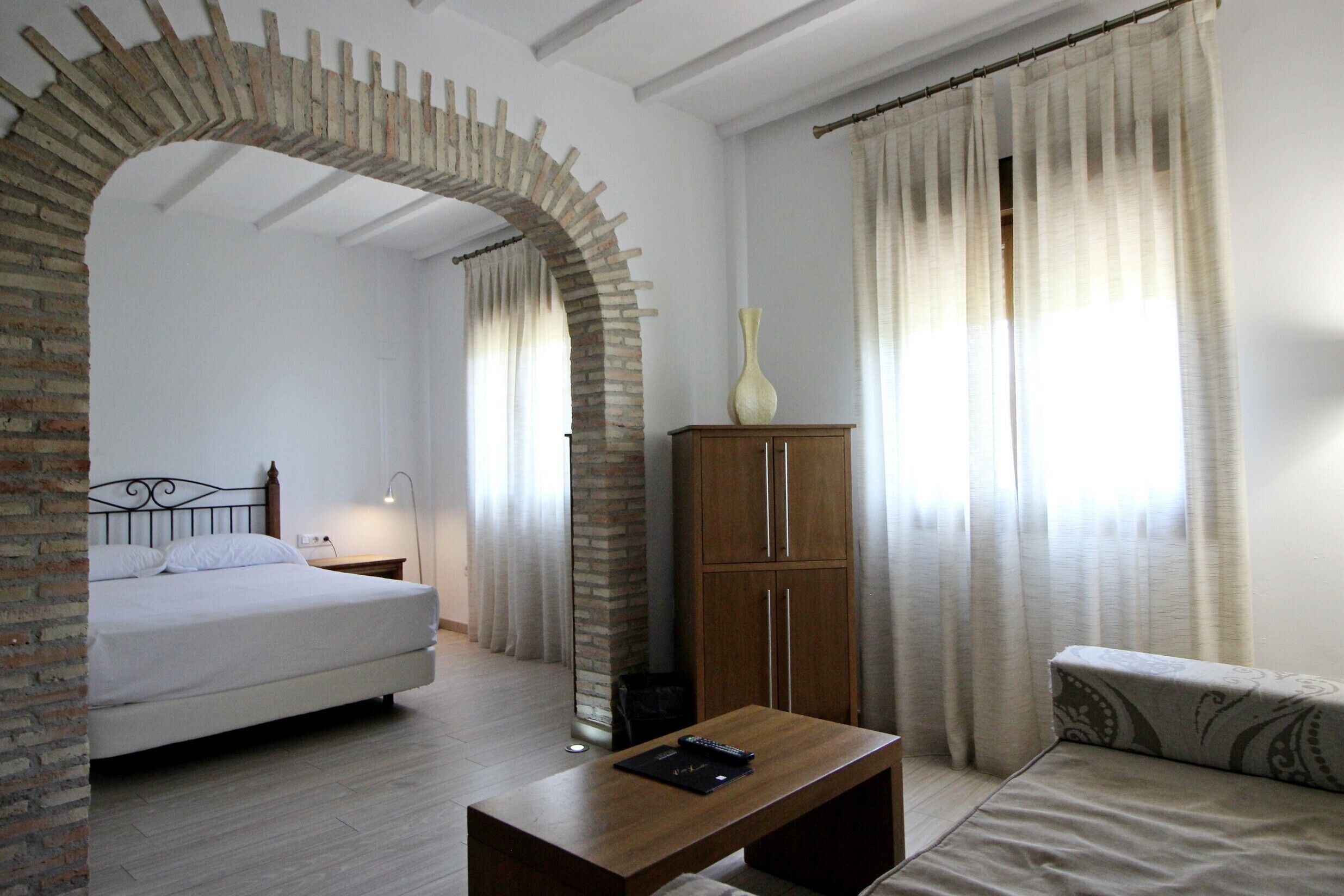 A bedroom with a bed, a wooden nightstand, a bedside table with a remote control, a wooden cabinet, and a sofa.